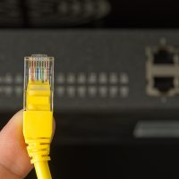 A internet cable that is being pictured in front of the internet switch that is behind the yellow A internet cable that is being pictured in front of the internet switch that is behind the yellow