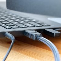 Power and hdmi cables, and wireless dongle USB mouse receiver on side of laptop on wooden table Power and hdmi cables, and wireless dongle USB mouse receiver on side of laptop on wooden table